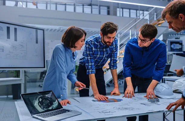 Fotografie von vier Personen. die über einen auf den Tisch liegenden Plan diskutieren.